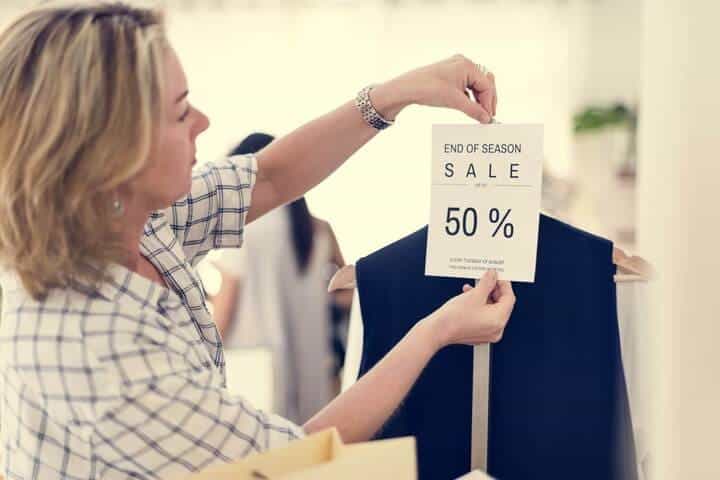 woman hanging a 50% sale sign up on clothing. 