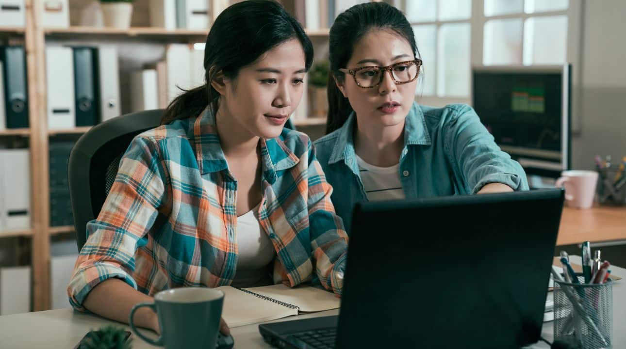 Picture showing to Asian women colleagues working together in front of a laptop computer.